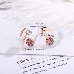 Rose gold cherry earrings with cat eye stones and pink rhinestones on a white feather