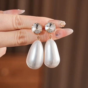 Gros plan de boucles d'oreilles perles gouttes avec cristaux tenues à la main