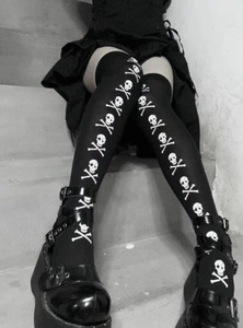 Detail of black over-the-knee socks featuring white skull and crossbones print