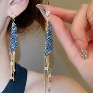 Detailed view of elegant long gold tassel earrings with blue crystals worn by a model
