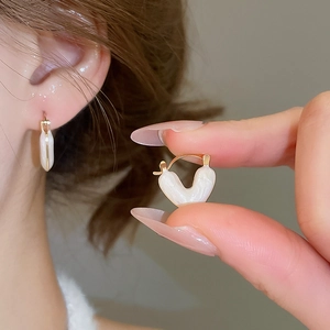 Close-up of golden heart-shaped earrings with white enamel finish and snap closure