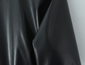 Detail of premium black faux leather texture and soft draped folds of the long coat