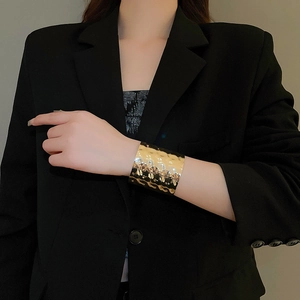 Close-up of a wide gold metal cuff bracelet with hammered texture on a model's wrist