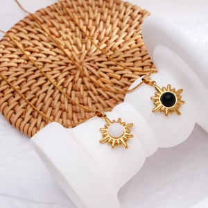 Gold sunburst necklace with black and white stone pendants on a white display pedestal