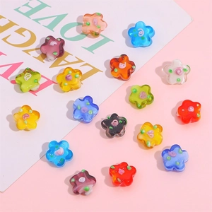 Colorful glass flower beads for DIY jewelry making scattered on pink background