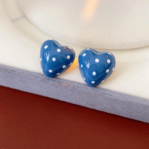 Close-up of blue heart-shaped earrings with white polka dots on a glossy finish