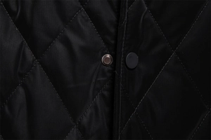 Detail of black quilted jacket featuring micro-grid fabric and matte snap button closure
