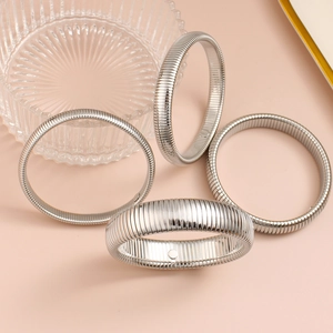 Brazaletes metálicos acanalados plateados pulidos sobre un fondo rosa suave