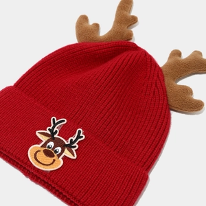 Detailed view of red knitted Christmas beanie with cute plush reindeer antlers and patch