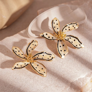Détail de boucles d'oreilles fleur, pétales crème à pois noirs et bords dorés