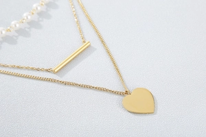 Detailed view of layered gold heart necklace and pearl chain on a textured grey background
