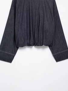 Detail of dark blue denim bomber jacket with elastic hem and white contrast stitching