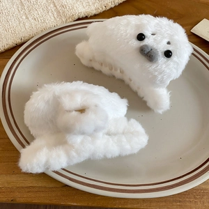 Detailed view of white plush seal hair claw clip with black eyes on a ceramic plate