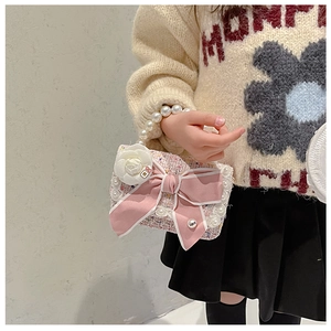 Close-up of pink tweed girl's bag with a large bow, camellia, and pearl bead handle