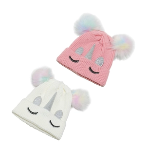 Détail de bonnets licorne tricotés rose et blanc avec pompons arc-en-ciel et corne