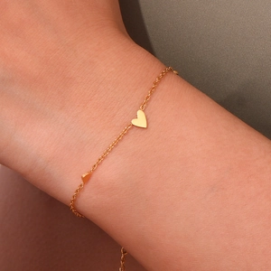 Detailed shot of delicate gold heart pendant chain bracelet worn on a female wrist
