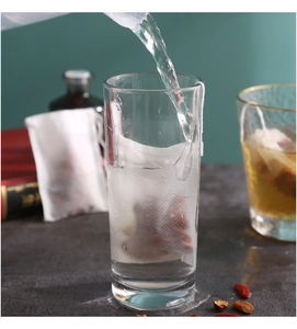 Detailansicht eines Einweg-Kräuterteebeutels mit Goji-Beeren in einem Glas beim Aufbrühen