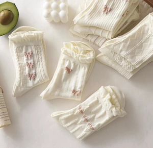 White knit socks with pink ribbon bows and ruffled cuffs in a professional flat lay