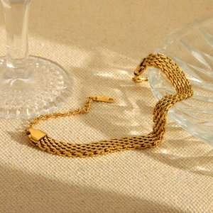 Elegant gold woven watchband style chain bracelet in stainless steel on a linen surface