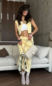 Close-up of pale yellow knit vest and skirt set with textured button details