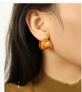 Close-up of a polished wide gold square hoop earring worn by a female model