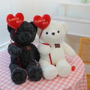 Close-up of black and white plush teddy bears with red heart balloon embroidery details