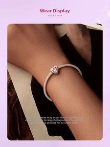 Gros plan d'un bracelet maille serpent argenté avec un pendentif cœur rose au poignet