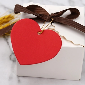 Close-up of white gift box with brown ribbon and a blank red heart-shaped paper tag