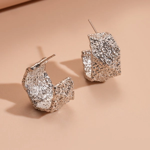 Close-up of silver C-shaped hoop earrings with unique hammered texture and metallic finish