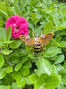 Detailed view of a gold bee brooch with pink rhinestones and small white floral wings