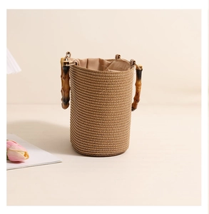 Detail of straw bucket bag with natural bamboo handle and drawstring lining on cream backdrop