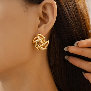 Close-up detail of twisted golden geometric flower stud earrings worn by a female model