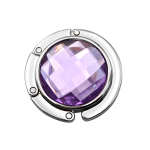 Macro view of a portable folding bag hook featuring a purple faceted crystal and silver frame