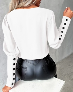 Detail of white puff sleeves with decorative black buttons and slim faux leather trousers