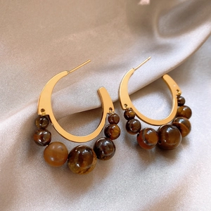 Detailed close-up of tiger eye beaded C-shaped earrings with vintage gold metal frame