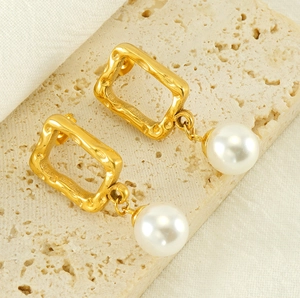 Macro detail of gold-plated square earrings with hammered texture and white pearls