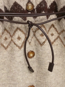 Detail of beige knit cardigan featuring brown geometric patterns and leather waist drawstring