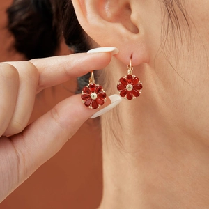 Elegant gold flower earrings with deep red teardrop stones shown on ear and held by hand