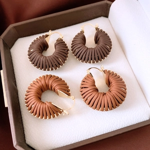 Détail de boucles d'oreilles pendantes rondes en cuir tressé avec attaches en métal doré