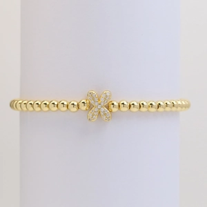 Macro detail of a gold beaded bracelet featuring a shimmering cubic zirconia flower charm