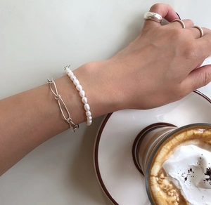 Detail of silver chain bracelet and pearl bracelet worn on hand with silver rings