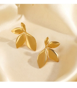 Macro shot of gold-finished leaf stud earrings on elegant beige silk fabric background