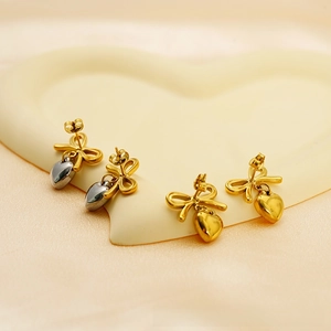 Detailed view of two pairs of gold bowknot stud earrings with silver and gold heart charms