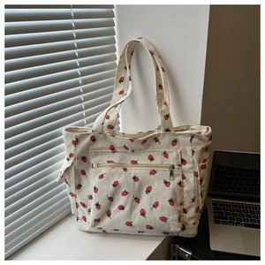 Detailed view of beige corduroy tote bag featuring red strawberry print and zipper pocket