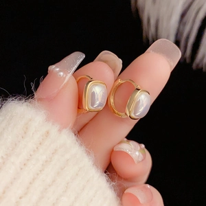 Minimalist square pearl earrings in gold frame shown from a hand-held macro perspective