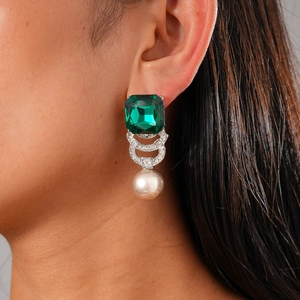 Macro view of emerald-cut green gem and large pearl drop earrings on model's ear