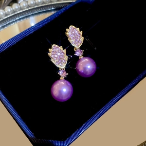 Macro shot of gold bow earrings with pink-purple rhinestones and large purple pearls