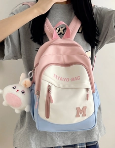 Girl wearing a tricolor patchwork school backpack with a cute white rabbit pendant