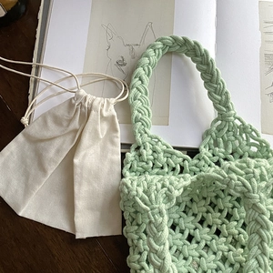 Handwoven light green tote bag with beige drawstring pouch on an artistic book background