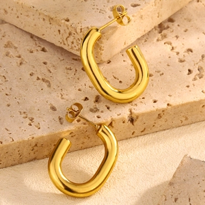 Detailed view of chunky U-shape gold hoop earrings on minimalist beige stone background